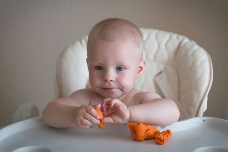 Children creativity. the baby is trying to sculpt from orange clay. Cute little boy mould from plasticine on table.の写真素材