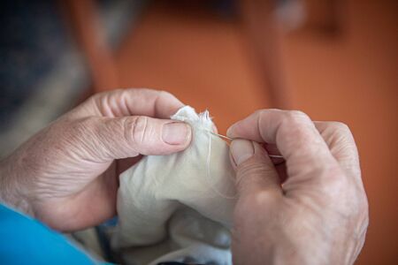 an elderly woman sews torn clothes. close-up of women's hands with thread and needle. the concept of poverty.の写真素材