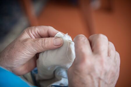 an elderly woman sews torn clothes. close-up of women's hands with thread and needle. the concept of poverty.の写真素材