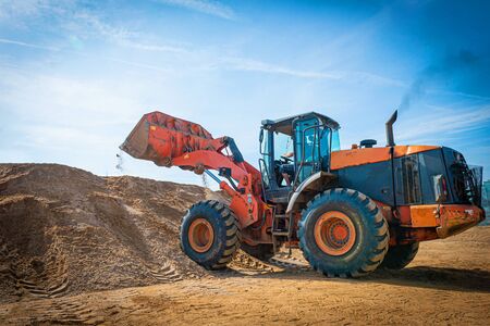 Yellow excavator on a construction site against blue sky. wheel loader at sandpit during earthmoving works.の写真素材