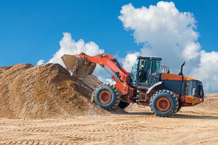 Backhoe loader or bulldozer - excavator with clipping path on a background with blue sky and clouds. work on construction site or sand pit.の写真素材