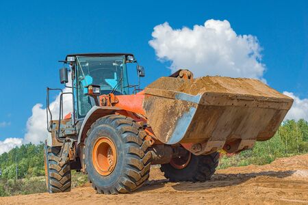 Backhoe loader or bulldozer - excavator with clipping path on a background with blue sky and clouds. work on construction site or sand pit.の写真素材