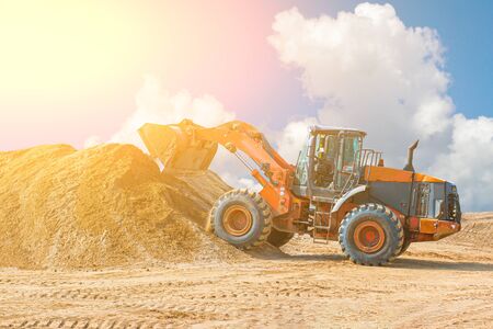Yellow excavator on a construction site against blue sky. wheel loader at sandpit during earthmoving works.の写真素材