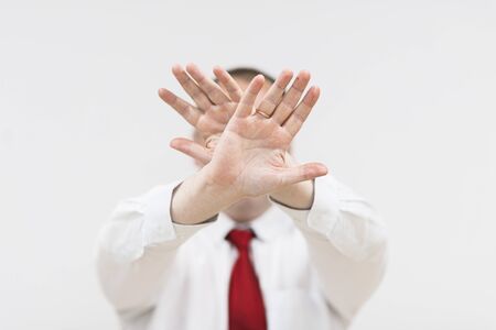 Shocked and terrified man forbids taking pictures of himself. Portrait of young man in shirt and red tie covering his face by hand and looking at camera isolated on white background.の写真素材