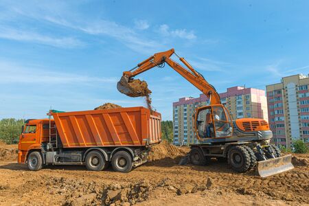 The modern excavator performs excavation work on the construction site. Excavator is loading excavation to the truck. Excavators hydraulic are heavy construction equipment consisting of a boom, dipper or stick , bucket and cab on a rotating platform.の写真素材