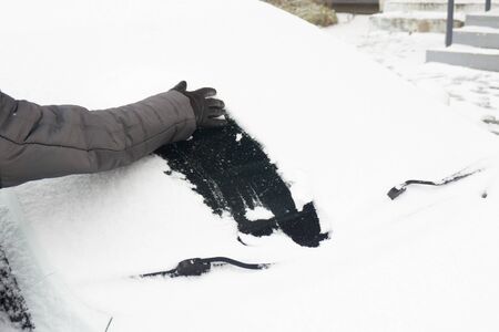 Woman cleaning car from snow with hand in glove. Snow-covered car windshield. parked car covered with snow during snowing in winter timeの写真素材
