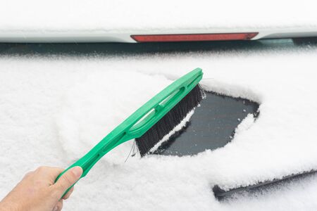 Man cleaning car from snow with brush. Snow-covered car windshield. parked car covered with snow during snowing in winter timeの写真素材