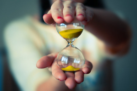 woman is holding hourglass in his hand. Life time passing concept. Sand running through the bulbs of...