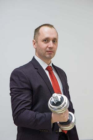 Portrait of confident businessman lifting dumbbell over light backgroundの写真素材