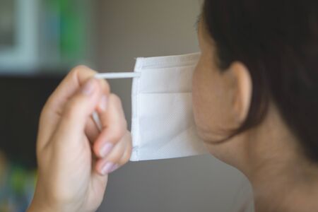 A woman puts on a medical mask while at home in isolation. Rear view. Protecting your own health during the quarantine period. Ncov-19 coronavirus pandemicの写真素材