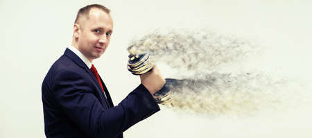 Businessman in black suit holding a silver dumbbell in the right hand. the dumbbell disappears like sand in the windの写真素材
