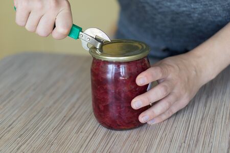 Closeup of woman opening a can in a kitchen with old style tin opener.の写真素材