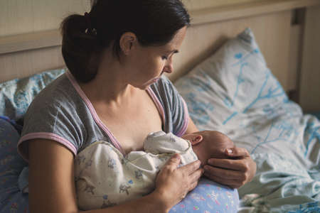 Young woman breast feeding her baby in bedroom. Mom nursing newborn girl.の写真素材