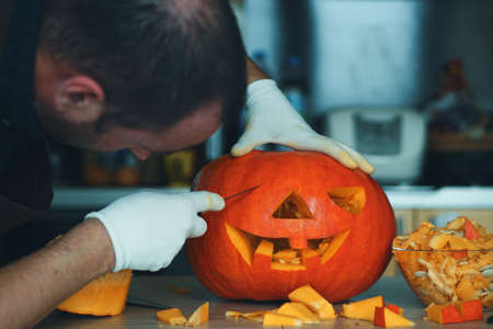 Man making Halloween pumpkin head jack lantern on wooden table at home, closeupの写真素材