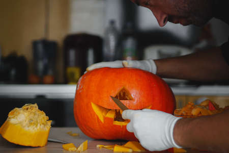 Man making Halloween pumpkin head jack lantern on wooden table at home, closeupの写真素材