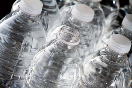 One open plastic bottle of water and other bottles closed on black backgroundの写真素材