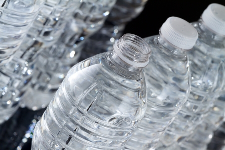 One open plastic bottle of water and other bottles closed on black backgroundの写真素材