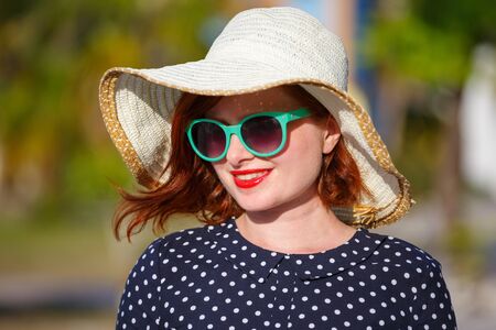 Red-haired girl in a hat and sunglasses on the background of the seaの写真素材