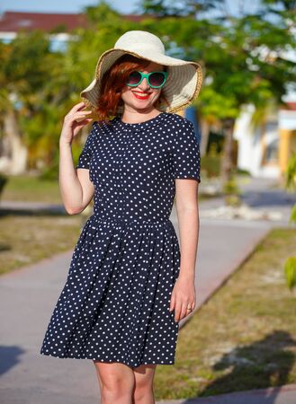 Young woman in polka-dot dress and straw hat on background of the palmsの写真素材