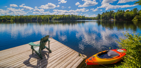 Chair sitting on a wood dock facing a calm lake with a red canoeの写真素材