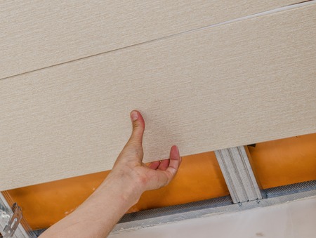 A worker installs panels beige siding on the facade of the houseの写真素材