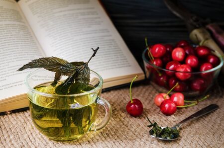 Still mint tea in a glass cup with cherries and a book on sackingの写真素材