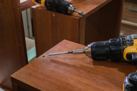 Assembling furniture from chipboard, using a cordless screwdriver, close up.
