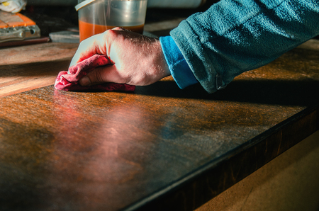 Carpenter paints tinted wood furniture details with wax for wood brush, close-upの写真素材