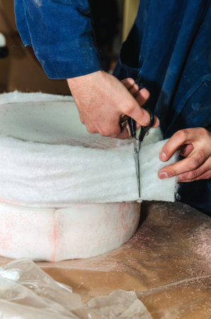 The master cuts with scissors blanks from sintepon for upholstery of upholstered furniture in the workshop, close-upの写真素材