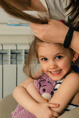 A little girl plays with her toy while she gets her hair done at home.の写真素材