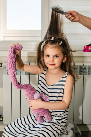 A little girl plays with her toy while she gets her hair done at home.の写真素材