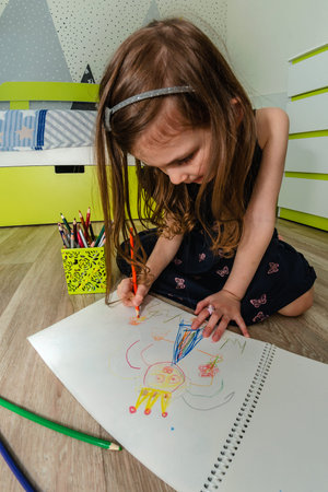 Little girl draws with pencils on the floor in her room.