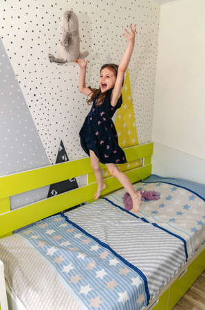 A little girl is jumping and playing in her room on the bed and laughing.の写真素材