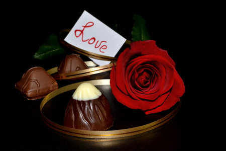 The studio red rose with golden ribbon, chocolate candy on a black background. Valentine's day backgroundの写真素材