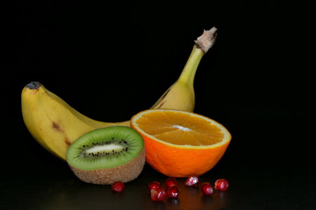 Kiwi fruit, orange, banana and pomegranate seeds on a black background. Space for textの写真素材
