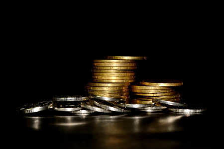 Stack of golden coins and heap of silver coins on black background. Space for textの写真素材
