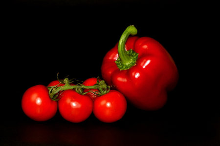 Studio photo branch of cherry tomatoes and red paprika isolated on black backgroundの写真素材