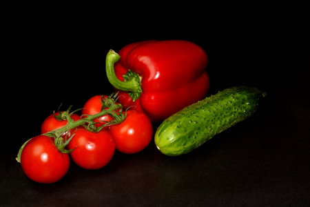 Fresh organic diet vegetables on black background. Branch of cherry tomatoes, red paprika and cucumberの写真素材