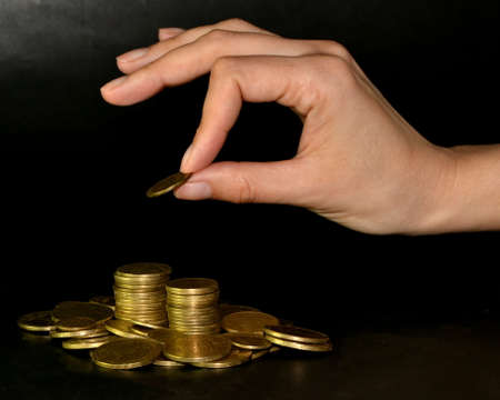 Saving money concept by adding a gold coin to a pile of coinsの写真素材