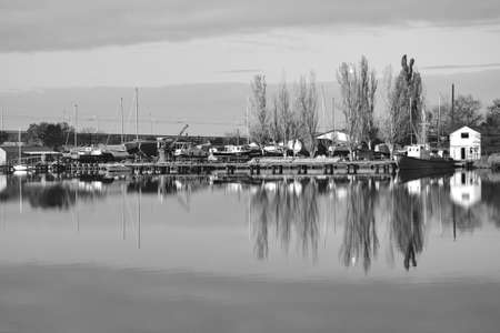 Black and white picture. Autumn reflections at the river.Beautiful landscape with trees and boats at the riverの写真素材