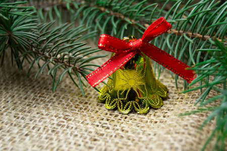 Christmas bell toy and branch of christmas tree on a burlap backgroundの写真素材