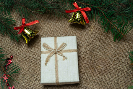 Christmas bell toys and branch of christmas tree with giftbox on a burlap background