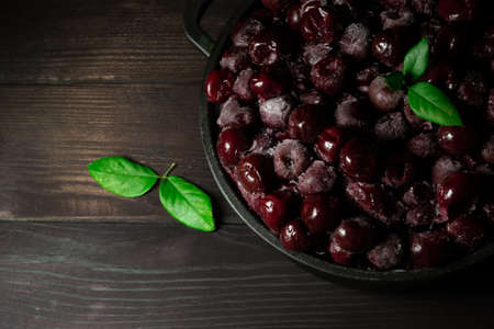 A lot of frozen cherry without sticks in the bowl on a wooden black background. Vitamins and a healthy diet. Copy spaceの写真素材