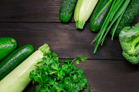 Organic green vegetables and herbs for cooking on dark wooden background with space for text. Top view. Concept of healthy, vegetarian, diet food.の写真素材