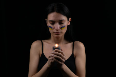 Patriotic ukrainian woman with burning candle are praying for Ukraine. dark background