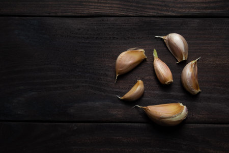 Garlic cloves on dark wood texture. Space for text. top view