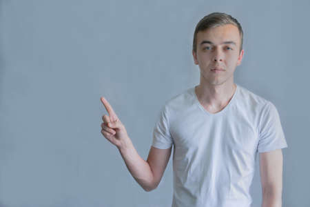 Young handsome man wearing casual white t-shirt pointing something on his side with his hand over gray backgroundの写真素材
