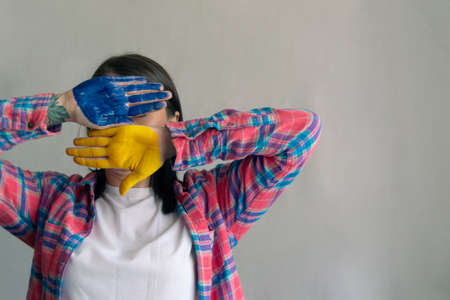 a woman covers her face with her hands in the paint of the color of the flag of Ukraine Space for textの写真素材