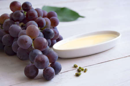 Grape seed oil in a plate near blue grapes and green leaves on white wooden table. Spa, bio, eco products concept.の写真素材