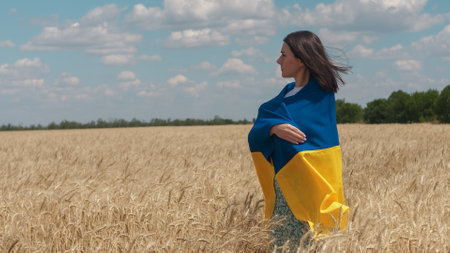 Ukrainian patriotic woman stands in wheat field with blue-yellow flag of Ukraine. Back view. Copy spaceの写真素材